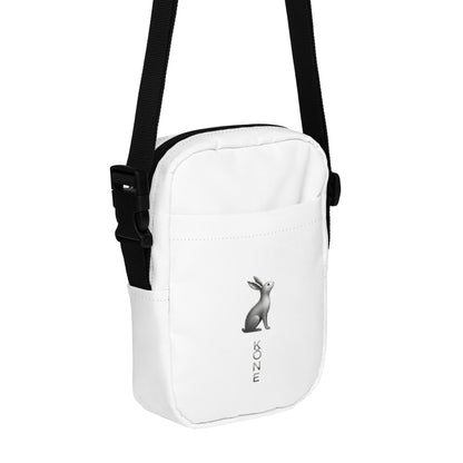 Bandolera KÖNE blanca con logo gris metalizado, diseño vertical minimalista y correa negra ajustable.
