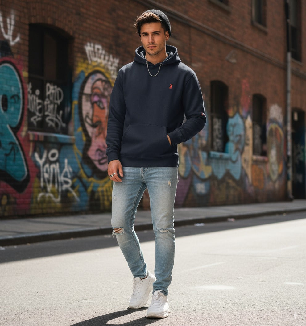  Hombre con sudadera azul marino KÖNE y pantalón tejano, estilo urbano casual en interior moderno.