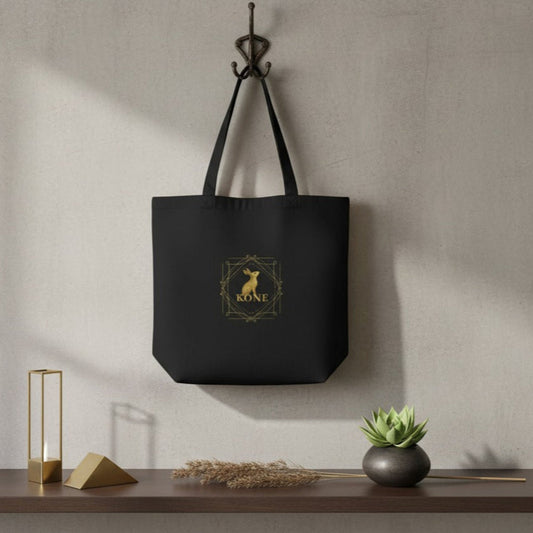 Bolsa tote negra KÖNE colgada sobre pared beige con luz natural y decoración minimalista