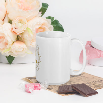 Vista lateral de la taza KÖNE blanca con diseño dorado y fondo decorativo con flores y dulces.