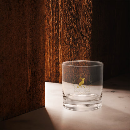 Vaso KÖNE con logo dorado iluminado en fondo cálido de madera