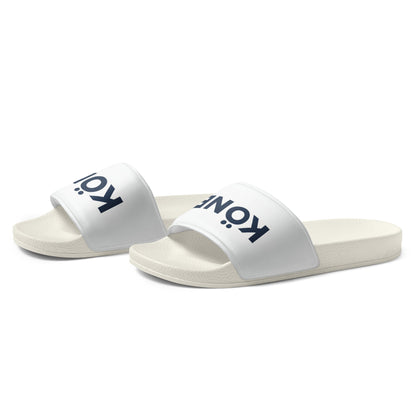Sandalias KÖNE blancas con logo negro, vista lateral mostrando suela texturizada y diseño ergonómico